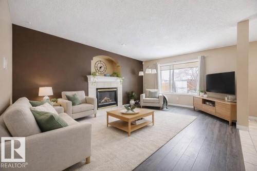The living area features a gas fireplace with a tiled surround and mantel, a broad window, dark wood-style flooring, and a light-colored area rug - 7 Doucette Place, St. Albert, AB - Indoor Photo Showing Living Room With Fireplace