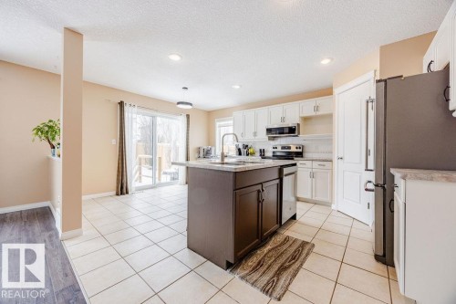 The kitchen features an island with a sink, white cabinetry, and stainless steel appliances - 7 Doucette Place, St. Albert, AB - Indoor Photo Showing Kitchen