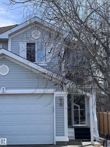 The property features light blue siding, a white garage door, and a front entry with dark steps and a storm door - 7 Doucette Place, St. Albert, AB - Outdoor