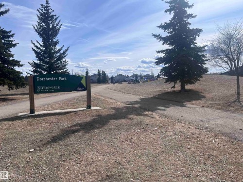 Community park featuring a prominent sign for "Dorchester Park", mature evergreen trees, and walking paths - 7 Doucette Place, St. Albert, AB - Outdoor With View