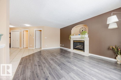 Living space featuring light-toned flooring, a fireplace with a stone surround, and warm-toned walls - 7 Doucette Place, St. Albert, AB - Indoor Photo Showing Living Room With Fireplace