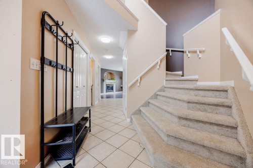 Entryway featuring tiled flooring, a carpeted staircase with white handrails, and a hallway leading to a room with a visible fireplace - 7 Doucette Place, St. Albert, AB - Indoor Photo Showing Other Room