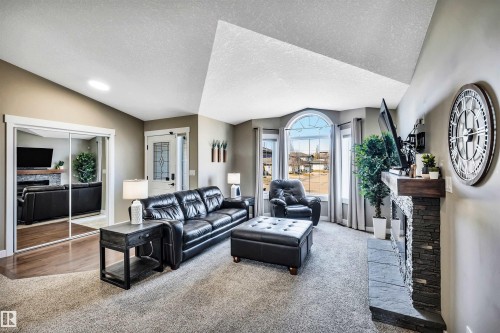 The inviting living area features a stone-clad fireplace with a wooden mantel, large bay windows with an arched top, and soft carpeting - 5201 40 Avenue, Beaumont, AB - Indoor Photo Showing Living Room
