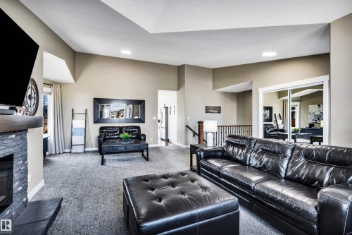 Living area featuring vaulted ceilings, a stone fireplace, and carpeted flooring - 5201 40 Avenue, Beaumont, AB - Indoor Photo Showing Living Room With Fireplace