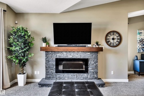 The living area features a natural stone fireplace with a wooden mantel, set against neutral-toned walls and carpeted flooring - 5201 40 Avenue, Beaumont, AB - Indoor Photo Showing Living Room With Fireplace