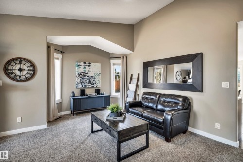 This living area features a neutral color palette, carpet flooring, and a large window - 5201 40 Avenue, Beaumont, AB - Indoor Photo Showing Living Room