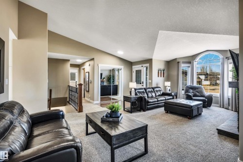 Spacious living area featuring vaulted ceilings, a large arched window providing natural light, and carpeted flooring - 5201 40 Avenue, Beaumont, AB - Indoor Photo Showing Living Room