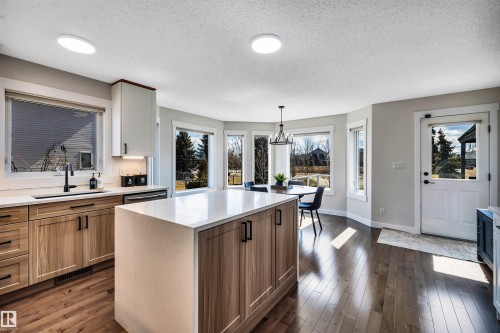 The kitchen features hardwood floors, a central island with a light-colored countertop, and light wood cabinetry with black hardware - 5201 40 Avenue, Beaumont, AB - Indoor Photo Showing Kitchen