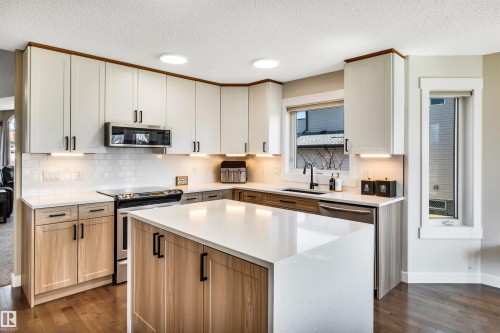 The kitchen features white shaker-style upper cabinetry with under-cabinet lighting, natural wood lower cabinetry, and a central island with a white countertop - 5201 40 Avenue, Beaumont, AB - Indoor Photo Showing Kitchen With Upgraded Kitchen