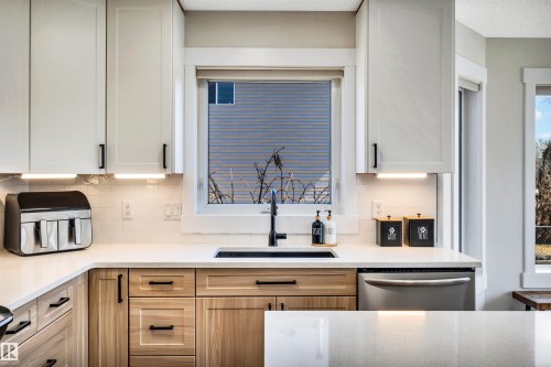The kitchen features light-colored upper cabinetry with dark handles, natural wood lower cabinetry, and a white countertop - 5201 40 Avenue, Beaumont, AB - Indoor Photo Showing Kitchen