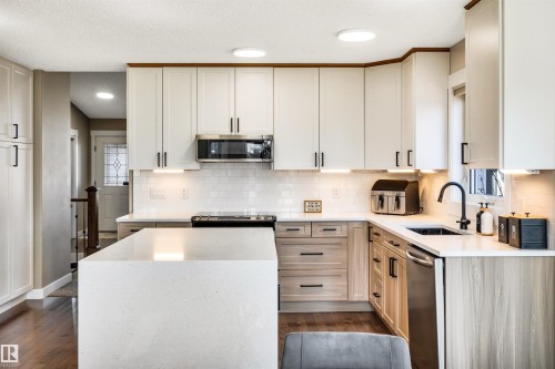 The kitchen features white shaker style cabinets, a large island with a light-colored countertop, and dark hardwood flooring - 5201 40 Avenue, Beaumont, AB - Indoor Photo Showing Kitchen With Upgraded Kitchen