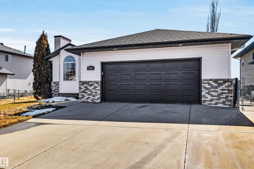 This property features a light-colored exterior with brick accents, a dark-colored garage door, and a paved driveway - 5201 40 Avenue, Beaumont, AB - Outdoor