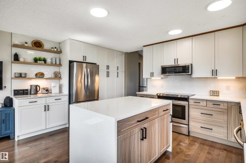 The kitchen features hardwood floors, a central island with a light-colored countertop, and a stainless steel refrigerator - 5201 40 Avenue, Beaumont, AB - Indoor Photo Showing Kitchen With Upgraded Kitchen