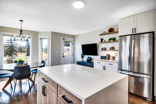 The kitchen features an island with a light-colored countertop and a stainless steel refrigerator - 5201 40 Avenue, Beaumont, AB - Indoor