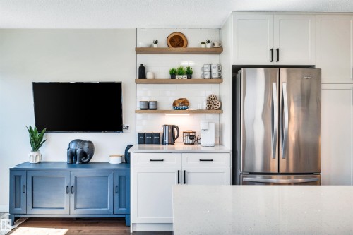 The property features a kitchen area with white cabinetry, a stainless steel refrigerator, and a white subway tile backsplash - 5201 40 Avenue, Beaumont, AB - Indoor Photo Showing Other Room