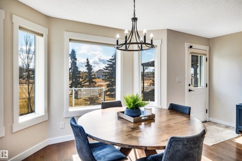 Dining area featuring a round wooden table, a black metal chandelier, and large windows offering views of the outdoors - 5201 40 Avenue, Beaumont, AB - Indoor Photo Showing Dining Room
