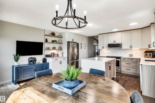 The kitchen features stainless steel appliances, a center island with a waterfall countertop, and white and wood-toned cabinetry - 5201 40 Avenue, Beaumont, AB - Indoor