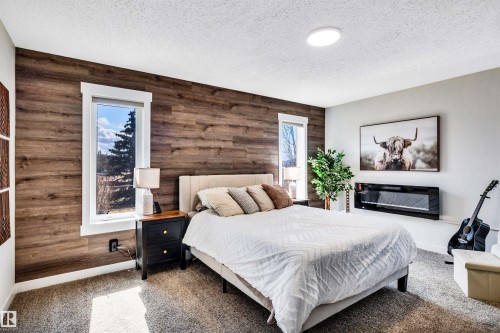 This bedroom features a striking wood-paneled accent wall with two windows providing natural light - 5201 40 Avenue, Beaumont, AB - Indoor Photo Showing Bedroom