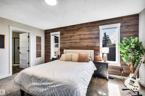 This room features a textured accent wall, two windows with white trim, and light-colored carpeting - 5201 40 Avenue, Beaumont, AB - Indoor Photo Showing Bedroom
