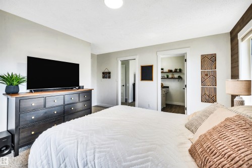 This inviting room features light-colored walls, carpeted flooring, and a window with a wood-paneled accent wall beside it - 5201 40 Avenue, Beaumont, AB - Indoor Photo Showing Bedroom