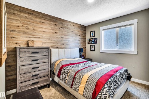 This bedroom features a striking wood-paneled accent wall, neutral-toned painted walls, and carpeted flooring - 5201 40 Avenue, Beaumont, AB - Indoor Photo Showing Bedroom