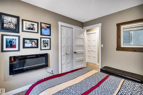 This room features a wall-mounted electric fireplace, neutral wall colors, and a window with a wood frame - 5201 40 Avenue, Beaumont, AB - Indoor Photo Showing Bedroom