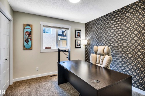 The room features a window with white trim, a dark patterned accent wall, and carpeting - 5201 40 Avenue, Beaumont, AB - Indoor Photo Showing Office