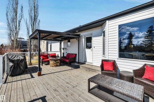 This property features an expansive outdoor deck with a pergola, a stone fire pit, and a large picture window on the exterior wall - 5201 40 Avenue, Beaumont, AB - Outdoor With Deck Patio Veranda With Exterior
