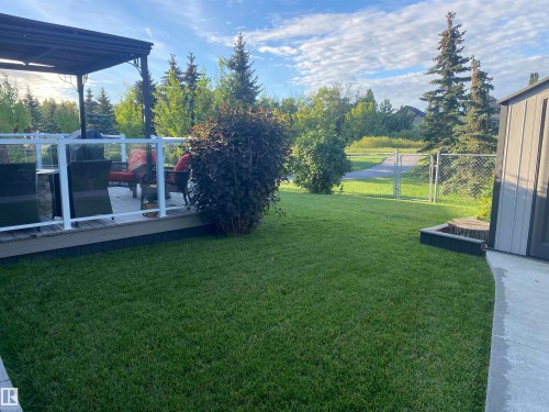 The property features a spacious lawn, a wooden deck with a white railing and a dark colored pergola, and a storage shed - 5201 40 Avenue, Beaumont, AB - Outdoor