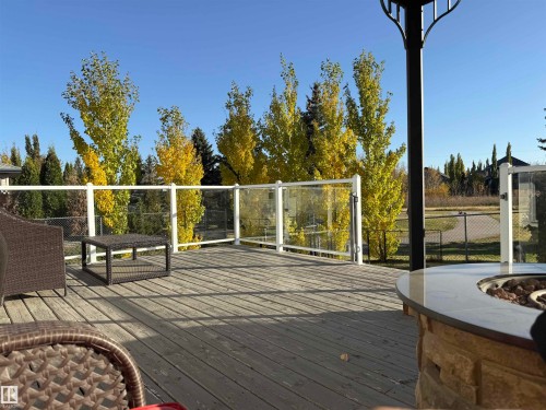 Expansive outdoor deck with glass railings, a built-in fire feature with a stone base, and views of surrounding trees - 5201 40 Avenue, Beaumont, AB - Outdoor