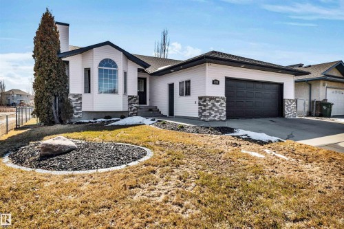 This property features a single-story structure with white siding and stone accents, a dark roof, and a two-car garage with a dark door - 5201 40 Avenue, Beaumont, AB - Outdoor
