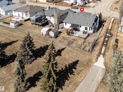 The property features an extensive backyard with mature trees, a deck, a patio, a fire pit, and two storage sheds - 5201 40 Avenue, Beaumont, AB - Outdoor