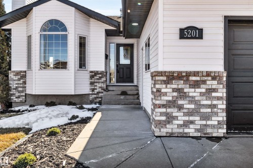 The property features a white exterior with brick accents, an arched bay window, and an attached garage - 5201 40 Avenue, Beaumont, AB - Outdoor