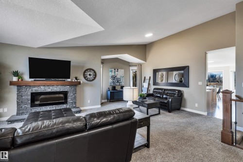 This living area features a stone fireplace with a wood mantle, carpeted floors, and a vaulted ceiling - 5201 40 Avenue, Beaumont, AB - Indoor Photo Showing Living Room With Fireplace