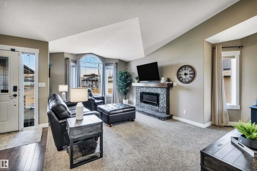 Inviting living area featuring vaulted ceilings, a stone-accented fireplace with a wood mantle, and a bay window with an arched transom - 5201 40 Avenue, Beaumont, AB - Indoor Photo Showing Living Room With Fireplace