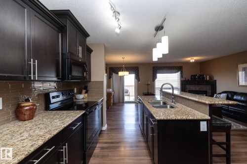 The kitchen features dark wood cabinetry, granite countertops, and a tile backsplash - 130 Kirpatrick Way, Leduc, AB - Indoor Photo Showing Kitchen With Double Sink With Upgraded Kitchen