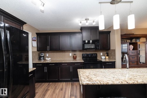 The kitchen features dark wood cabinetry, a black refrigerator, and a black range with an overhead microwave - 130 Kirpatrick Way, Leduc, AB - Indoor Photo Showing Kitchen With Upgraded Kitchen