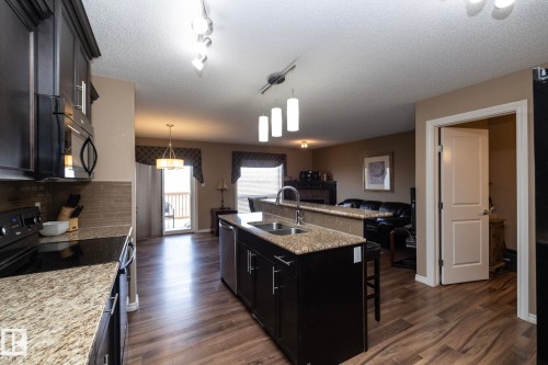 The kitchen features dark wood cabinetry, granite countertops, and stainless steel appliances - 130 Kirpatrick Way, Leduc, AB - Indoor Photo Showing Kitchen With Double Sink