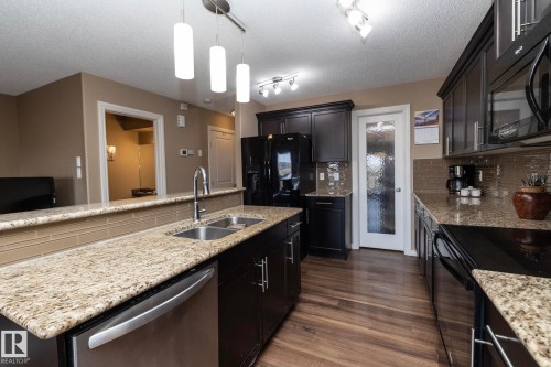 The kitchen features dark wood cabinetry, granite countertops, and a tile backsplash - 130 Kirpatrick Way, Leduc, AB - Indoor Photo Showing Kitchen With Double Sink With Upgraded Kitchen
