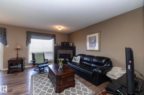 Living area featuring wood-look flooring, a fireplace with a tiled surround, and a window with blinds - 130 Kirpatrick Way, Leduc, AB - Indoor Photo Showing Living Room With Fireplace