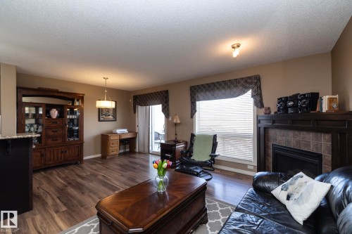 The living area features wood-style flooring, a fireplace with a tiled surround, and a sliding glass door leading to the exterior - 130 Kirpatrick Way, Leduc, AB - Indoor Photo Showing Living Room With Fireplace
