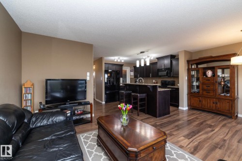 Open concept living area featuring wood-look flooring, a kitchen with dark cabinetry and light-toned countertops, and a kitchen island with seating - 130 Kirpatrick Way, Leduc, AB - Indoor Photo Showing Living Room