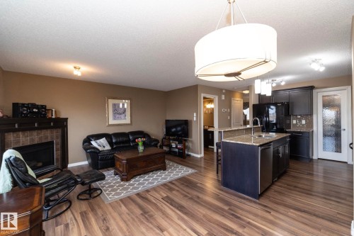 Open concept living space featuring wood flooring, a fireplace with a tiled surround, and an island kitchen - 130 Kirpatrick Way, Leduc, AB - Indoor With Fireplace