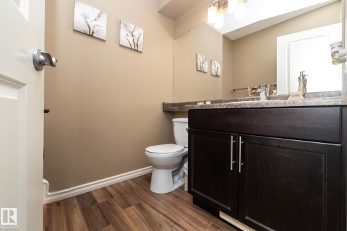 The bathroom features a dark wood vanity with a light-colored countertop, a white toilet, and wood-look flooring - 130 Kirpatrick Way, Leduc, AB - Indoor Photo Showing Bathroom