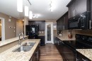 The kitchen features dark wood cabinetry, granite countertops, and stainless steel appliances - 130 Kirpatrick Way, Leduc, AB  - Indoor Photo Showing Kitchen With Double Sink 