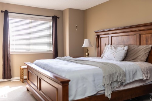 The bedroom features a large window with blinds and drapes, and a substantial wooden bed frame with a prominent headboard - 130 Kirpatrick Way, Leduc, AB - Indoor Photo Showing Bedroom