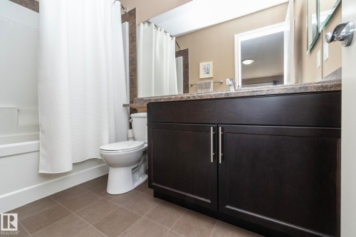 Bathroom featuring a dark wood vanity with a light-colored countertop, a white toilet, and a white bathtub with a shower curtain - 130 Kirpatrick Way, Leduc, AB - Indoor Photo Showing Bathroom