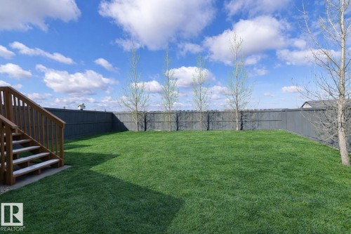 The property features a spacious lawn, a wooden fence, and several young trees - 130 Kirpatrick Way, Leduc, AB - Outdoor