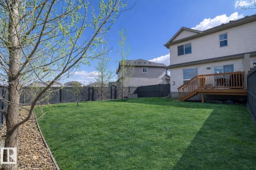 The property features a spacious backyard with a well-maintained lawn and a wooden deck, ideal for outdoor enjoyment - 130 Kirpatrick Way, Leduc, AB - Outdoor With Deck Patio Veranda