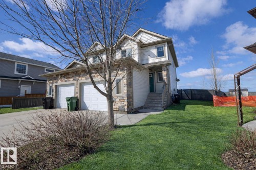 The property features a two-car garage with a concrete driveway, a well-maintained lawn, and a stone facade accenting the exterior - 130 Kirpatrick Way, Leduc, AB - Outdoor